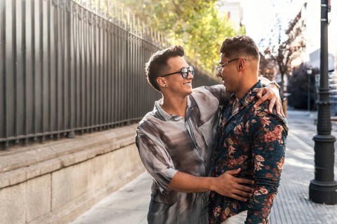 A joyful latin gay couple shares a warm embrace and smiles while walking on a sunny day in the
