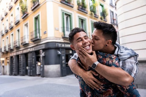 A joyful latin gay couple embraces in a cheerful moment while exploring the lively streets of
