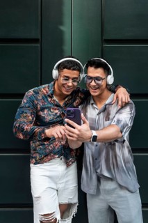 A happy couple in stylish outfits share a joyful moment with headphones and a smartphone. They