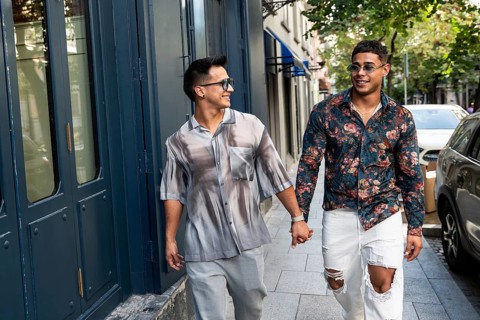 A happy latin gay couple holds hands while strolling down a lively city street in Madrid. They wear