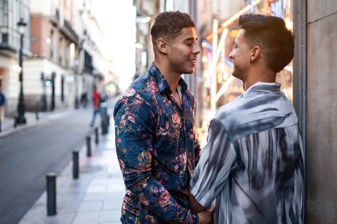 A joyful latin gay couple shares an intimate moment on a lively street in Madrid, highlighting