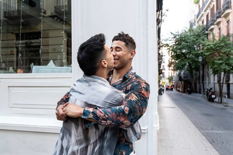 A joyful latin gay couple embraces and shares a tender moment on a charming street in Madrid. The