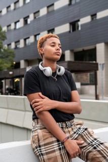 A confident young hispanic transgender with short hair wearing headphones and plaid pants, leaning