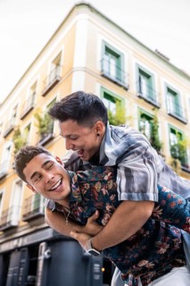 A joyful latin gay couple share a playful piggyback ride in the vibrant streets of Madrid. The warm