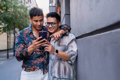 A joyful latin gay couple stands close together on a sunny street in Madrid, sharing a moment as