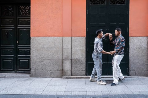 A joyful latin gay couple shares a moment of affection on a lively street in Madrid. Their