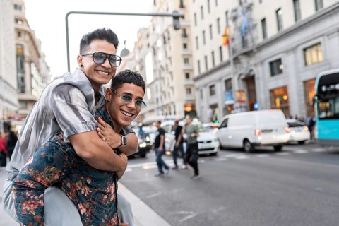 A happy latin gay couple smiles and embraces in the bustling streets of Madrid, showcasing love and