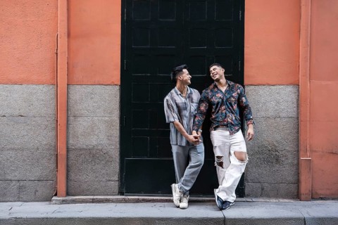 A joyful latin gay couple shares a tender moment holding hands, standing in front of a colorful