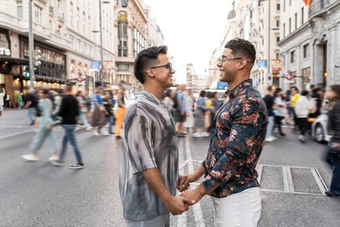 A joyful latin gay couple holds hands and smiles at each other amidst the hustle and bustle of a