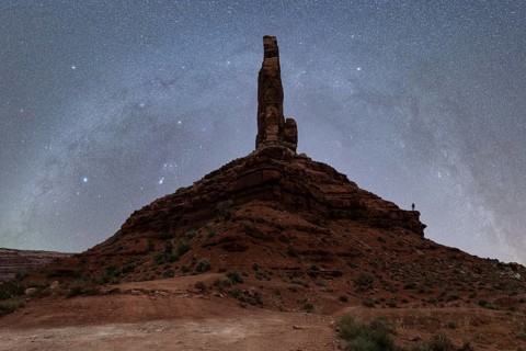 Unrecognizable silhouette of a person standing on a massive rock formation under the starry sky of