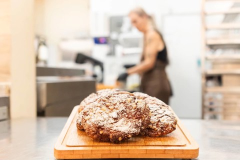 A close-up of freshly baked Italian cookies on a wooden board in a bustling bakery, with a blurred
