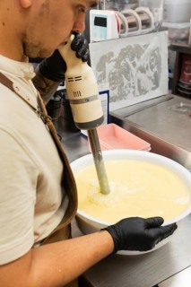 A skilled baker uses an immersion blender to prepare batter in a large bowl The setting is a
