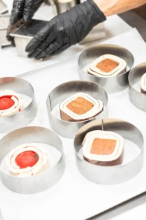 A close-up of a baker's hands wearing gloves, skillfully preparing Italian pastries in metal rings