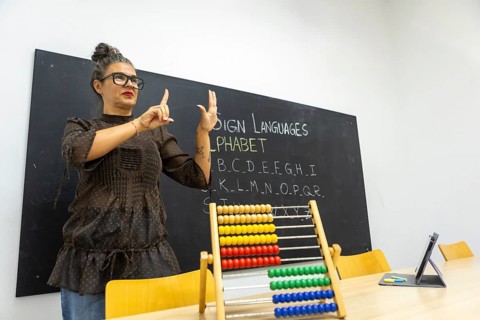An instructor demonstrates sign language, using hand gestures to teach the alphabet The classroom
