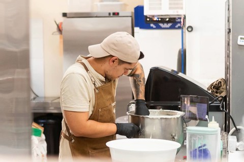 A dedicated baker in a traditional Italian bakery mixes dough in a stainless steel bowl, showcasing