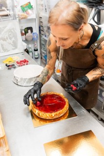 An artisan baker decorates a glossy fruit tart with fresh berries in an Italian bakery kitchen The