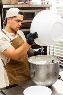 A focused baker in an apron and cap prepares dough in a busy Italian bakery kitchen The setting