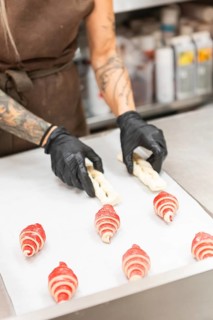A skilled artisan wearing gloves crafts intricate pastries on a preparation table in an Italian