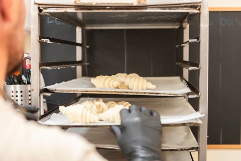 A baker places raw croissants onto a baking rack in an Italian bakery The scene captures the