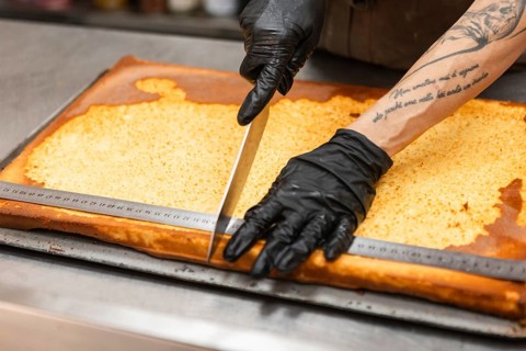 An artisan wearing gloves skillfully slices a traditional Italian cake with a large knife The large