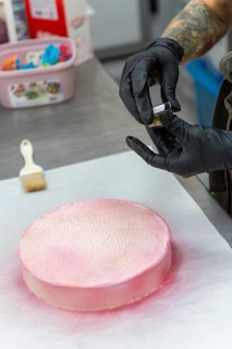 A skilled baker wearing gloves applies pink icing and gold dust to a cake in an Italian bakery The
