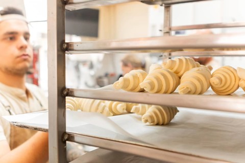 A baker carefully places freshly rolled croissants on a rack in a bustling Italian bakery The dough