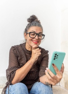 A woman with glasses uses a smartphone for a video call, focusing on learning sign language She is