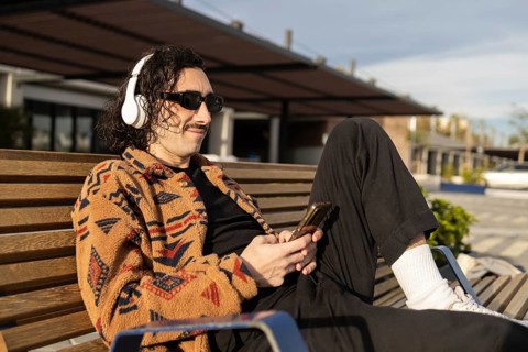 A man relaxes on a bench, wearing headphones and sunglasses, enjoying music on a sunny day He wears