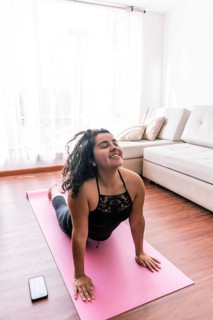 A young latin woman performs yoga on a pink mat in her cozy living room, enjoying a peaceful moment