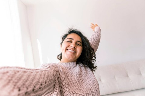 A young latin woman smiles joyfully while stretching in her comfortable home environment She wears