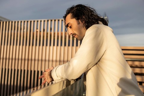 A man in a light shirt leans on a railing, captured in soft evening light His thoughtful expression