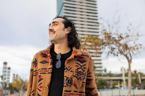 A stylish man with a patterned coat and sunglasses smiles confidently in an urban setting A modern