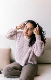 A young latin woman with curly hair relaxes on a couch at home, wearing a cozy sweater and