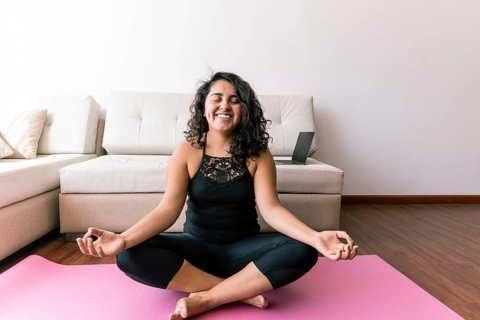 A young latin woman sits peacefully on a yoga mat in a serene living room She practices yoga,