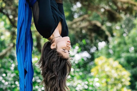 Aerial acrobat performs elegant moves on blue fabric amidst lush greenery in a Bogota park The