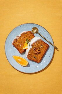 Slices of carrot cake loaf topped with cream cheese frosting, garnished with walnuts, rosemary, and