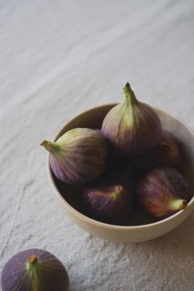 A rustic ceramic bowl filled with ripe, purple figs placed on a textured linen tablecloth,