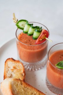 A refreshing glass of gazpacho garnished with cucumber, tomato, and bell pepper on a skewer Served