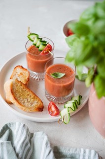 Two glasses of fresh gazpacho garnished with cucumber and tomato skewers, served with toasted bread