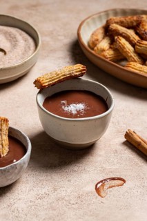 Homemade churros dipped in rich chocolate sauce, sprinkled with sugar and cinnamon, presented on a