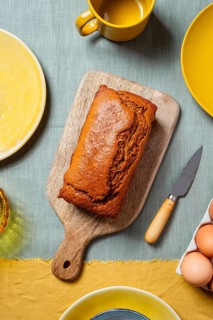 A freshly baked carrot cake loaf sits on a wooden board surrounded by a warm, autumn-themed table