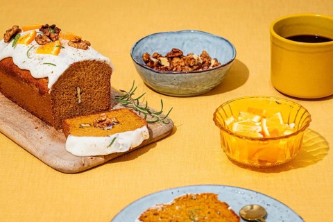 A moist carrot cake loaf topped with cream cheese frosting, garnished with walnuts and rosemary