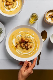 A creamy cauliflower curry soup garnished with croutons, rosemary, and drizzles of cream, served in