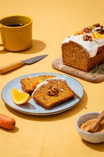 A tasty carrot cake loaf topped with creamy frosting and walnuts, presented on a yellow linen