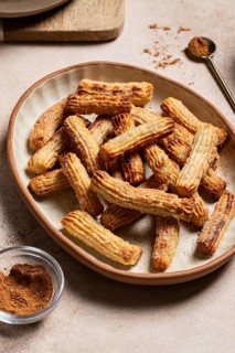 Homemade churros dusted with sugar and cinnamon, served on a ceramic plate alongside chocolate and