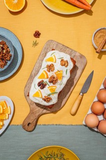 Carrot cake loaf topped with cream cheese frosting, orange slices, walnut, and rosemary Set on a