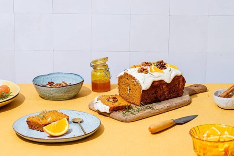 A mouthwatering carrot cake loaf topped with creamy cheese frosting, walnuts, and rosemary Vibrant