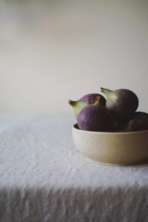 A close-up of fresh figs in a rustic bowl on a textured white tablecloth, creating a serene and