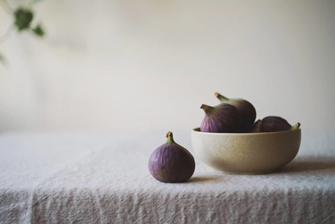 A collection of ripe figs in a ceramic bowl on a rustic tablecloth One fig is placed outside the