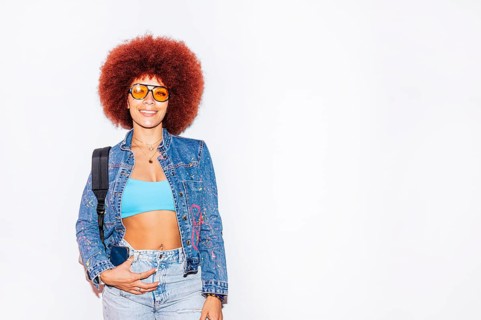 African descendant woman with a vibrant afro hair, smiling while wearing orange sunglasses and a